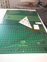Photo showing the large green Omnigrid cutting mat with rulers placed on top including rectangular and triangle rulers, with a paper note with $20.