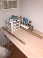 Wooden table holding plastic storage drawers, spray bottle, starch spray cans, brown craft paper rolls, and rulers aligned on the surface.