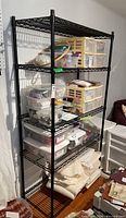 Front view of black metal shelving unit loaded with various storage bins, plastic containers, and folded fabrics.