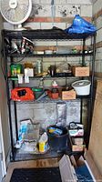 Full view of the black wire shelving unit holding various household and garden-related supplies in a concrete block room.