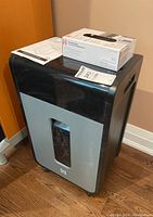 Paper shredder with shredder bags and manual on top, showing front transparent window and black-gray body.