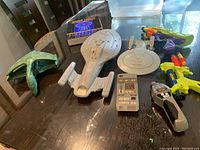 Overview photo of Star Trek models, toys, and blueprints book on a table showing Voyager, Enterprise, Bird of Prey models, tricorder, phaser, Nerf guns, and blueprint book.