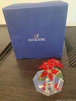Small Swarovski blue box with logo and small crystal poinsettia flower pot in front of it on dark surface.