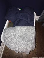 Photo of folded dark navy knit sweater with gray marled sweater below it in white basket on floor