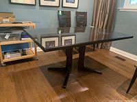 Wood dining table with dark wood finish and removable glass top from side view in room with hardwood floor and chairs.