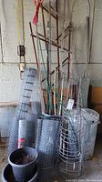 Overall view of the lot showing wire fencing rolls, tomato cages, trellis sections, black plastic pots, and metal garbage can.