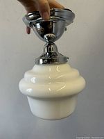 Photo showing chrome metal ceiling mount and white tiered glass shade held by hand from side angle, highlighting lamp design and condition.