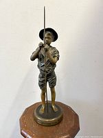 Front view of the patinated bronze fishing boy statue on wooden base showing facial features, clothing details and fishing rod.
