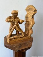 Front view of carved wood miner sculpture showing detailed miner figure operating pneumatic drill with helmet and stand.