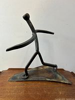 Side angle view of the steel abstract running man sculpture on wooden surface against white background.