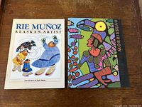Two vintage art books side by side: 'Rie Munoz Alaskan Artist' and 'Norval Morrisseau Shaman Artist' with colorful covers featuring Indigenous art.