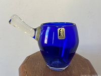 Cobalt blue glass vase with clear handle placed on wooden surface showing label and shape
