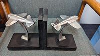 Front view showing both silvered metal airplane bookends with black slate bases positioned on a fabric chair, illustrating the streamlined design and size.