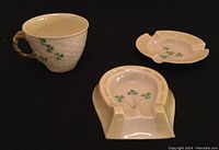 Three piece set of Belleek Irish porcelain including horseshoe ashtray, round ashtray, and tea cup with shamrocks.