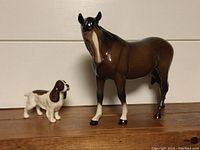 Front view of the horse and dog figurines together on a wooden surface against a plain backdrop