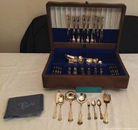 Full set in Birks wooden chest with blue felt lining, showing knives in lid slots and other pieces in main storage area plus laid out serving pieces and polishing cloth.
