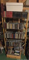 Full view showing wooden 5-shelf CD rack filled with over 200 CDs and a white storage box on top.