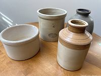 Overall view of all 4 crocks together on wooden table showing size, shape, and glaze colors.