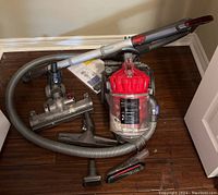 Dyson DC32 vacuum and multiple attachments laid out on wooden floor, showing overall contents of the lot