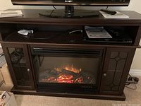 Full frontal view of dark brown mantel with electric fireplace insert lit and TV stand above