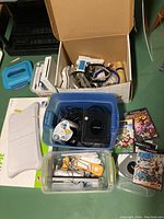 Overview photo showing multiple gaming items including Nintendo GameCube console, Wii Fit board, several controllers, and physical game cases.