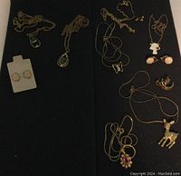 Collection of gold tone necklaces and earrings laid out on black fabric, showing variety of pendants and earrings with stones and enamel accents.