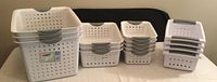 Full view of different sized Sterilite plastic storage baskets stacked and grouped by size in white with gray handles.
