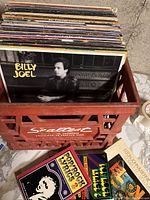 Red plastic crate filled with vinyl LPs showing a Billy Joel album in front with two lyric books below