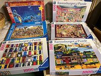 Photo shows all six Ravensburger 1000-piece puzzles grouped together, with colorful box art including Christmas scene and various scenes of cottages, doors, and indoor settings.