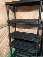 Photo of one black plastic shelving unit with five grid-style shelves and round support poles.