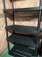 Close-up photo of one black plastic shelving unit with five adjustable shelves and vertical support poles.