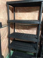 Photo showing one black plastic shelving unit with 5 slatted shelves, in a corner against walls with a brown-ish tone.