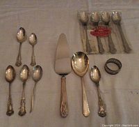 Wide view showing all spoons spread out including iced tea spoons still packaged, pie lifter, large serving spoon, and napkin ring.