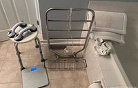 Photo showing towel warmer, shower stool, digital scale, bath mats, and sink decor on tiled bathroom floor near bathtub.