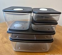 Stacked clear Tupperware Rock'n Serve microwave dishes with black lids and white vent valves showing various sizes including two 600 ml, one 1.5 L, one 3.5 L, and a divided meal dish.