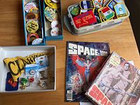 Photo shows multiple compartments containing vintage buttons, pins, and badges, plus Space 1999 puzzle and comic book on table.