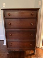 Front view of vintage wood tallboy dresser showing four drawers with wooden knobs and dark brown finish.