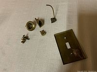 Six pieces of brass on a cloth surface showing various shapes and types including a light switch plate and small decorative pieces.