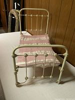 Doll bed fully assembled with pink blanket on top, showing front view of footboard and headboard with decorative round accents on rods.