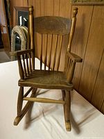 Front view of wooden child's rocking chair showing carved decorative upper backrest and spindle back and arms.