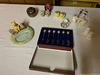 Wide view showing all items on table: ceramic Winnie the Pooh soap dish, three salt and pepper shaker sets, and boxed set of spoons.