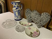 Front view of ceramic pitcher, two porcelain dishes, glass cover, crystal bowl, and two wicker hearts