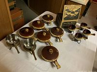 Full set of brown ceramic skillet-shaped dishes with lids and small matching bowls with metal stands, arranged on table, vintage Hull Oven Proof USA cookware.