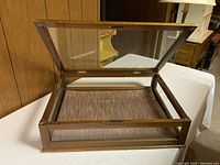 Top angled view of rectangular wood and glass display box with lid open showing inside lined with textured brown fabric.
