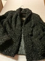 Black curly faux fur coat with pockets and lining shown from different angles on a bed.