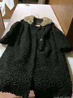 Black fur coat with light colored fur collar laid flat on surface.