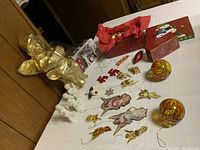 Photo showing a golden angel statue, flat vintage-style character decorations spread out, a red glitter decorative piece, and two large amber glass ball ornaments on a table.