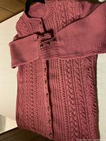 Front view of dusty rose handmade sweater showing button-up front, cable knit detailing, ribbed cuffs with decorative buttons.