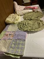 Photo of small patchwork quilt, two round ruffled pillow covers, pale yellow Columbia twin sheets folded on bed.