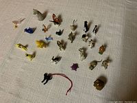 Overview of all 25 small animal and bird miniature figurines on fabric surface, showing various species and colors.